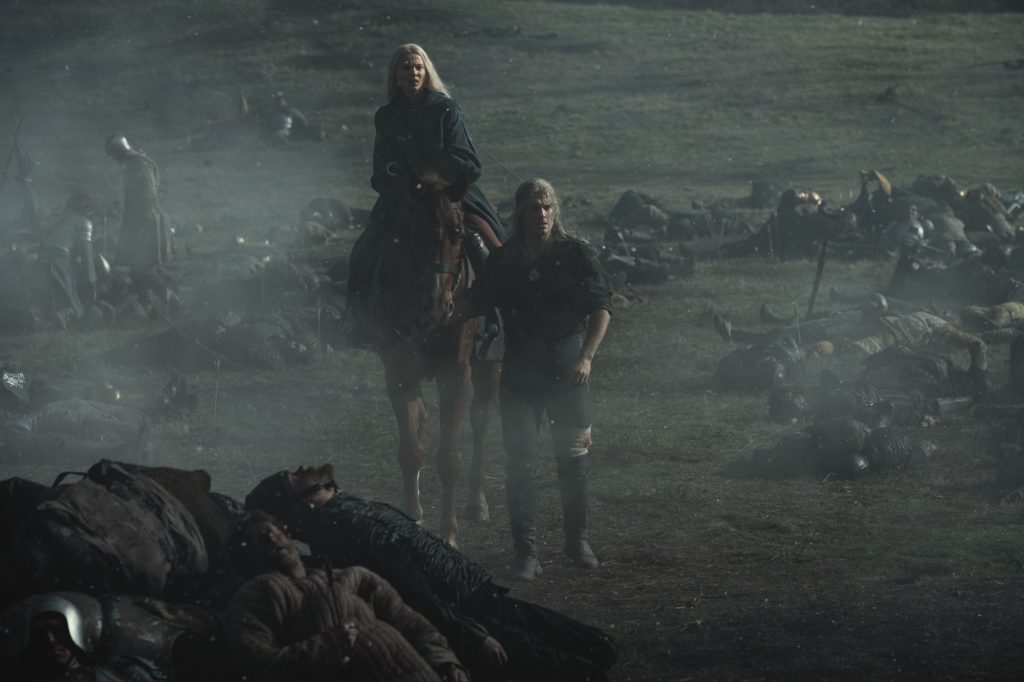 ciri em um cavalo e geralt a pé passando pelo campo de batalha de sodden